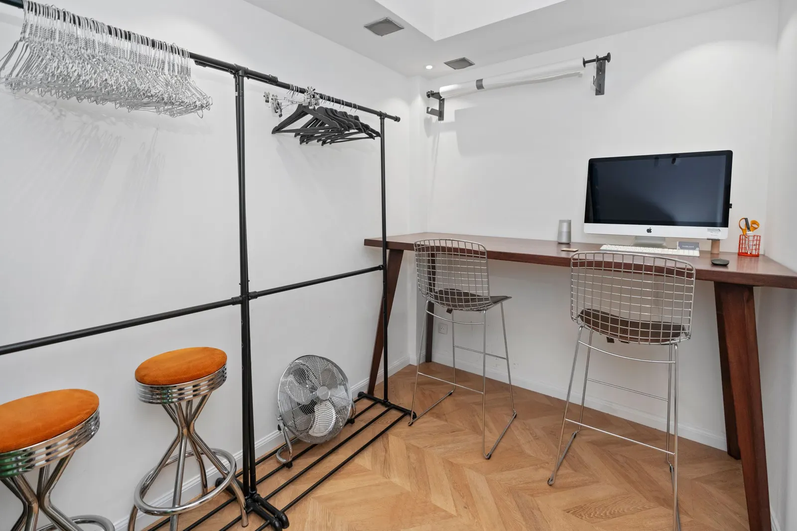 Espace vestiaire du studio avec deux portants à cintres et un bureau en bois